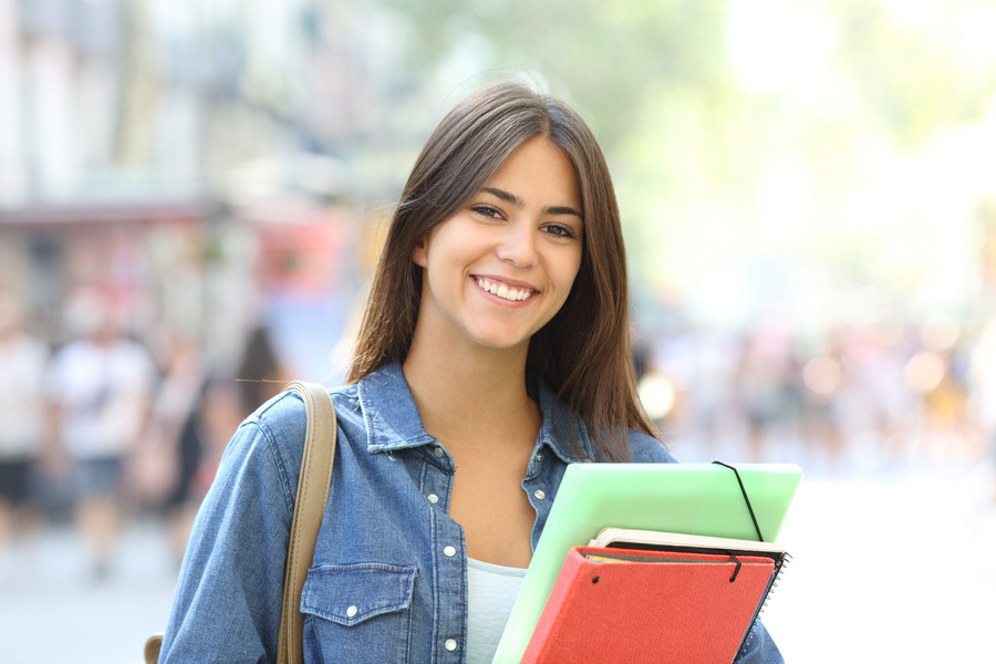 Happy student holding folders poses looking at camera in the street