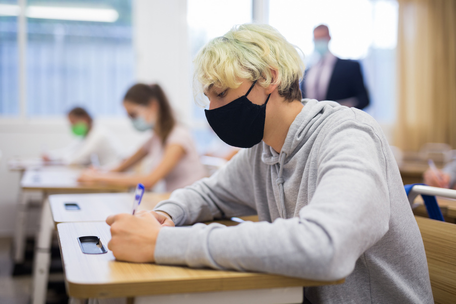 Portrait of teenager in protective face mask writing in workbook on lesson. New life reality during COVID pandemic