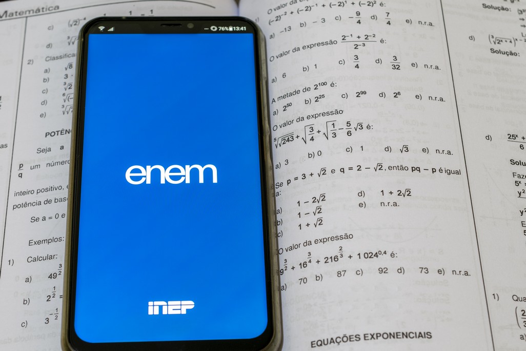 São Paulo, Brazil - December 3, 2020: cell phone with Enem application (national high school exam) and study book with math questions.