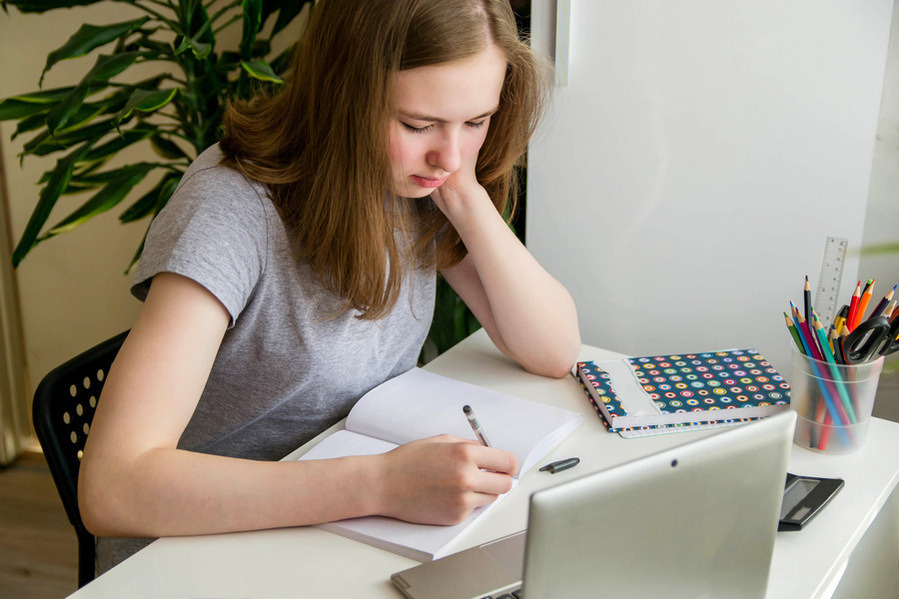 Distance learning online education. A schoolgirl is studying at a computer at home and doing school homework.