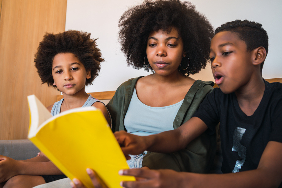 Portrait of Afro American mother reading a book to her children at home. Family and lifestyle concept.
