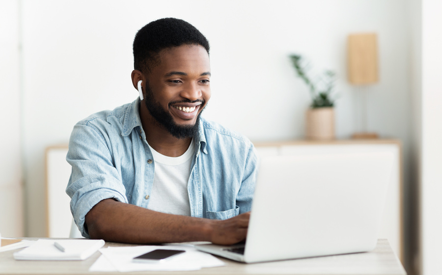 Smiling african-american guy in earphones studying foreign language online through video conference application, panorama with copy space