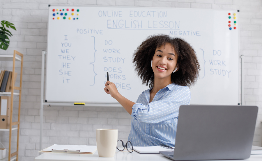 Modern education remotely. Cheerful young african american woman points to blackboard and explains rules of english online