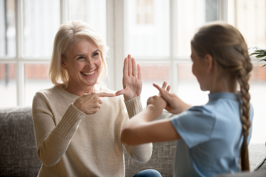Smiling senior woman grandmother make sign language talk gesturing with granddaughter at home, deaf dumb mute grandparent and grandchild speak using nonverbal communication, disabled people concept