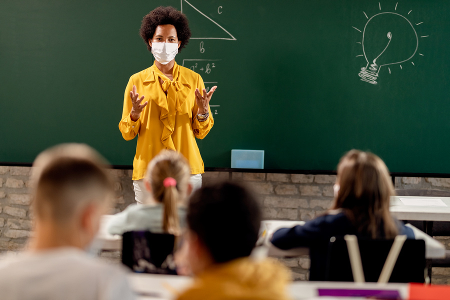 Black teacher with protective face mask teaching her students on a class at elementary school.