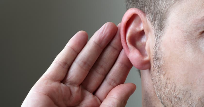 Homem com a mão levantada ao lado da orelha, sinalizando dificuldade de audição, surdez